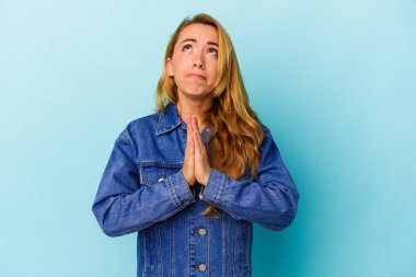 Mavi arka planda izole edilmiş beyaz bir kadın el ele tutuşup, ağzının kenarında dua ediyor, kendinden emin..