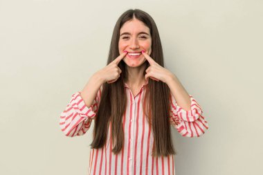 Sarı arka planda izole edilmiş genç beyaz kadın gülümsüyor, parmaklarını ağzına doğrultuyor..