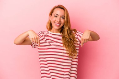 Beyaz tenli sarışın kadın pembe arka planda izole edilmiş, parmakları aşağıda, olumlu hisler içinde..