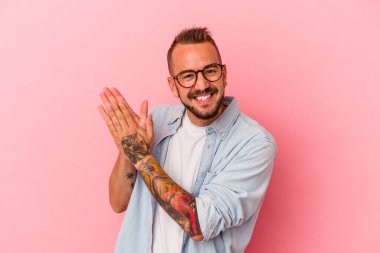 Pembe arka planda izole edilmiş beyaz dövmeli genç bir adam enerjik ve rahat hissediyor, ellerini ovuşturuyor..