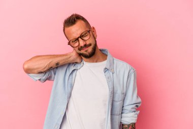 Pembe arka planda dövmeleri olan beyaz bir genç. Stresten dolayı boynu ağrıyor. Masaj yapıyor ve elle dokunuyor..