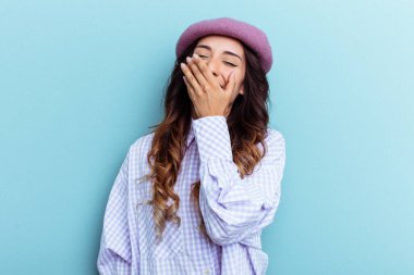 Genç Meksikalı bir kadın mavi arka planda izole edilmiş gülerek, kaygısız, doğal duygularla gülüyor..