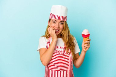 Kafkas dondurma üreticisi kadın elinde dondurma tutuyor mavi arka planda izole edilmiş tırnaklarını yiyor, gergin ve endişeli..