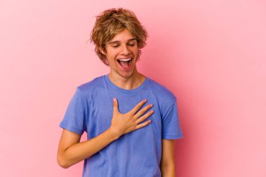 Pembe arka planda soyutlanmış beyaz makyajlı genç bir adam yüksek sesle gülüyor ve elini göğsüne koyuyor..