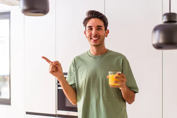 Joven Hombre Raza Mixta Bebiendo Jugo Naranja Cocina Sonriendo Señalando — Foto de Stock