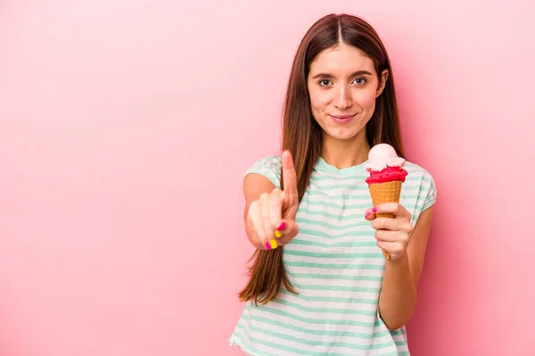 若いですCaucasian女性を持っていますアイスクリームを持っていますピンクの背景に隔離されましたナンバーワンを示しますとともに指 — ストック写真