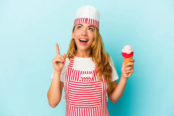 口を開けたまま逆さまに指差す青い背景にアイスクリームを持つ白人のアイスクリームメーカーの女性 — ストック写真