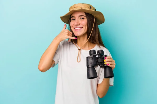 年轻的高加索探险家女人拿着一副蓝色背景的双筒望远镜 用手指做一个手机通话手势 — 图库照片