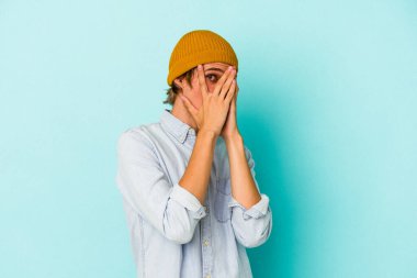 Makyajlı genç beyaz adam mavi arka planda izole edilmiş. Korkmuş ve gergin parmaklarıyla göz kırp..