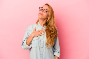 Beyaz tenli sarışın kadın pembe arka planda izole edilmiş yemin ediyor, elini göğsüne koyuyor..
