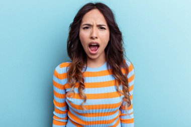 Mavi arka planda izole edilmiş genç Meksikalı kadın çok kızgın, öfkeli, hayal kırıklığına uğramış.