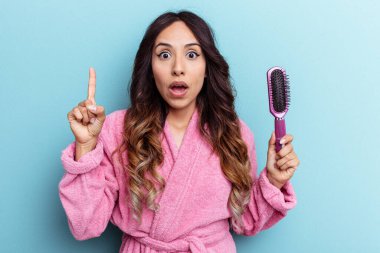 Bornoz giyen genç Meksikalı kadın mavi arka planda izole edilmiş bir fırça tutuyor. Bir fikri var, ilham verici bir kavram..