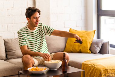 Genç melez adam kanepede oturmuş patlamış mısır yiyor.