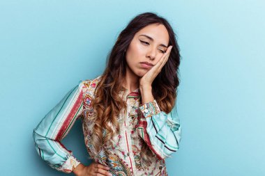 Mavi arka planda izole edilmiş genç Meksikalı kadın sıkılmış, yorgun ve dinlenmeye ihtiyacı var..