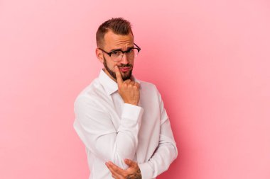 Pembe arka planda izole edilmiş dövmeleri olan genç, beyaz bir adam. Bir strateji planlıyor, nasıl bir iş kurulacağını düşünüyor..