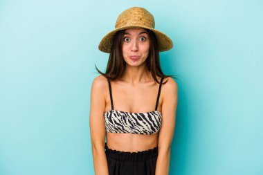 Genç, beyaz bir kadın kumsala gidiyor. Mavi arka planda izole edilmiş bir bikini giyiyor. Omuzlarını silkiyor ve gözleri açık..