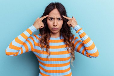 Mavi arka planda izole edilmiş genç Meksikalı kadın bir işe odaklanmış, işaret parmaklarını işaret ediyor..