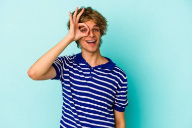Makyajlı genç beyaz adam mavi arka planda izole edilmiş, heyecanlı..