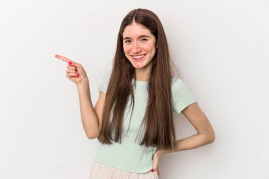 Beyaz arka planda izole edilmiş genç beyaz kadın işaret parmağıyla işaret ederek gülümsüyor..