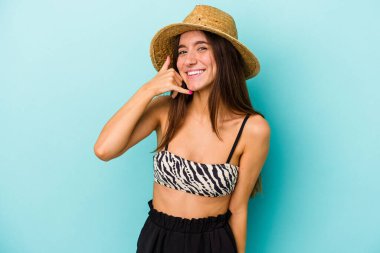 Genç beyaz bir kadın kumsala gidiyor. Mavi arka planda izole edilmiş bir bikini giyiyor. Cep telefonu hareketlerini parmaklarıyla gösteriyor..