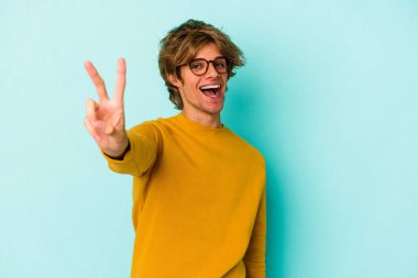 Mavi arka planda soyutlanmış beyaz makyajlı genç bir adam neşeli ve kaygısız parmaklarıyla barış sembolü gösteriyor..