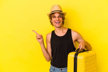 Makyajlı genç beyaz adam sarı arka planda izole bir şekilde seyahat edecek gülümseyecek ve boş alanda bir şey gösterecek..