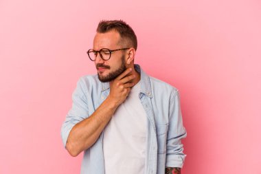 Pembe arka planda dövmeleri olan beyaz bir adam virüs ya da enfeksiyon yüzünden boğazında ağrı hissediyor..