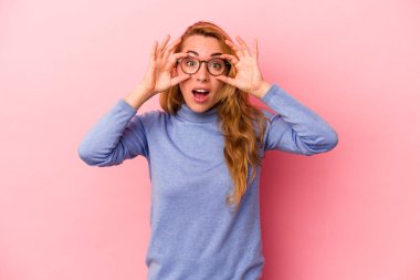 Pembe arka planda izole edilmiş beyaz tenli sarışın kadın bir başarı fırsatı bulmak için gözlerini açık tutuyor..