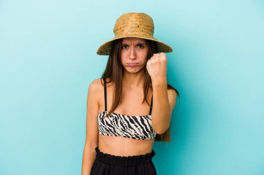 Genç beyaz kadın plaja gidiyor. Mavi arka planda izole edilmiş bir bikini giyiyor. Kameraya yumruğunu gösteriyor..