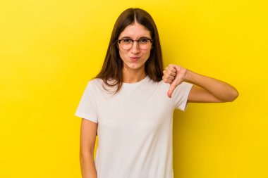 Sarı arka planda izole edilmiş genç beyaz kadın baş parmağını aşağı gösteriyor, hayal kırıklığı konsepti..