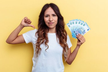 Sarı arka planda izole edilmiş banknotları tutan genç melez kadın gururlu ve kendinden emin hissediyor, örnek olarak..