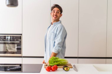 Genç melez adam öğle yemeği için salata hazırlıyor. Gülümsüyor, neşeli ve keyifli görünüyor..