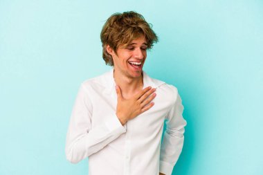 Mavi arka planda soyutlanmış beyaz makyajlı genç bir adam gülüyor, ellerini yüreğine koyuyor, mutluluk kavramını koruyor..
