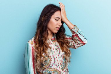 Mavi arka planda izole edilmiş genç Meksikalı kadın bir şeyi unutuyor. Alnına avuç içi ve kapalı gözlerle vuruyor..