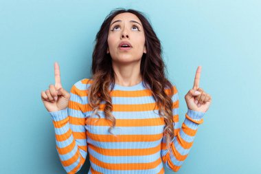 Mavi arka planda izole edilmiş genç Meksikalı kadın ağzı açık bir şekilde üst tarafı işaret ediyor..