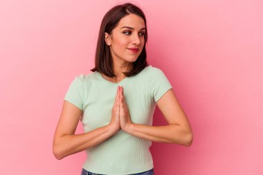 Pembe arka planda izole edilmiş genç beyaz kadın dua ediyor, bağlılık gösteriyor, dindar biri ilahi ilham arıyor..