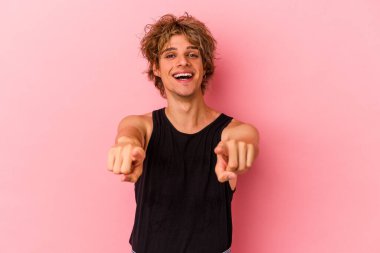 Makyajlı genç beyaz adam pembe arka planda izole edilmiş. Önü işaret eden neşeli gülümsemeler..