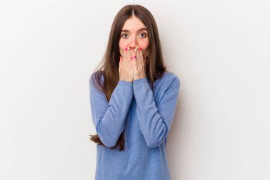 Beyaz arka planda izole edilmiş beyaz tenli genç bir kadın elleri endişeli bir şekilde ağzı örtüyor..