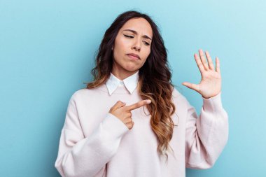 Mavi arka planda izole edilmiş genç Meksikalı kadın gülümseyerek beş numarayı parmaklarıyla gösteriyor..