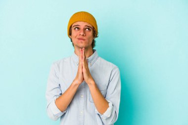 Mavi arka planda soyutlanmış beyaz makyajlı genç bir adam el ele tutuşarak dua ediyor, kendinden emin hissediyor..