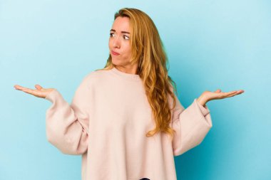 Mavi arka planda izole edilmiş beyaz bir kadın. Kafası karışmış ve omuz silkiyor. Kopya alanını tutmak için..