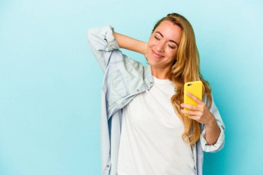 Kafkasyalı bir kadın cep telefonunu mavi arka planda izole edip kafasının arkasına dokunuyor, düşünüyor ve bir seçim yapıyor..