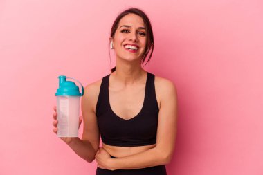 Pembe arka planda izole edilmiş protein içeceği içen beyaz bir kadın gülüyor ve eğleniyor..