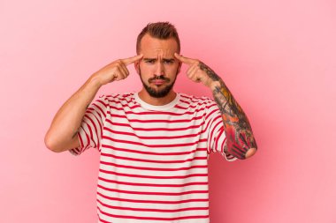 Pembe arka planda dövmeleri olan beyaz genç bir adam görevine odaklanmış, işaret parmaklarını işaret ediyor..