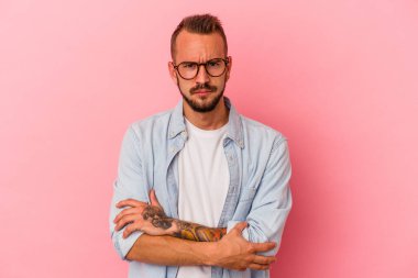Pembe arka planda izole edilmiş beyaz dövmeli genç adam alaycı bir ifadeyle kameraya bakıyor..