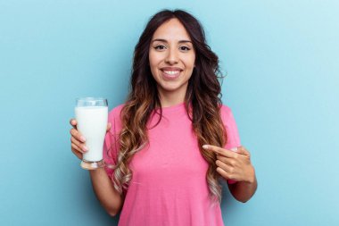Mavi arka planda bir bardak süt tutan genç bir ırk kadını tişört fotokopi alanını işaret ediyor, gururlu ve kendinden emin.