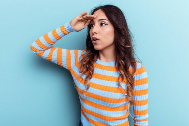 Mavi arka planda izole edilmiş genç Meksikalı kadın uzaklara bakıyor ve elini alnına koyuyor..