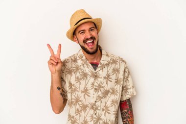 Yazlık giysiler giyen, beyaz arka planda izole edilmiş, neşeli ve tasasız bir barış sembolü gösteren dövmeli genç beyaz bir adam..