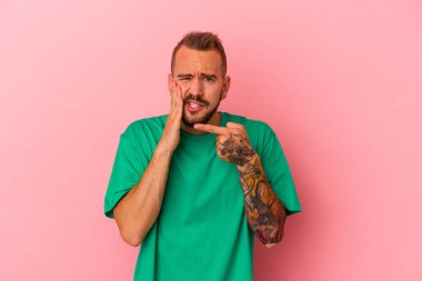 Pembe arka planda izole edilmiş dövmeleri olan beyaz bir genç adam. Güçlü bir diş ağrısı, azı dişi ağrısı var..