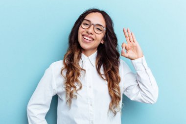 Mavi arka planda izole edilmiş genç Meksikalı kadın bir göz kırptı ve elleriyle iyi bir jest yaptı..